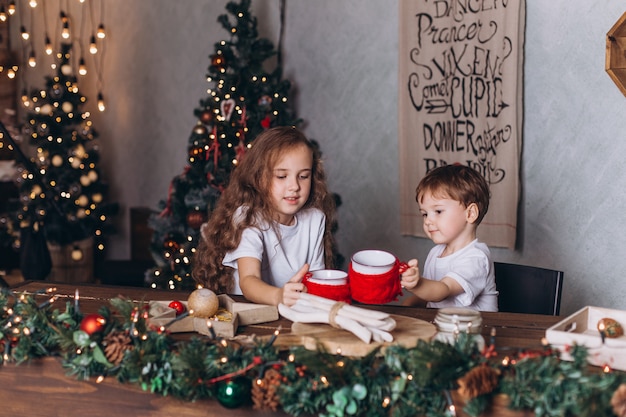 Crianças na decoração de Natal com chá em casa aconchegante com luzes coloridas do ano novo