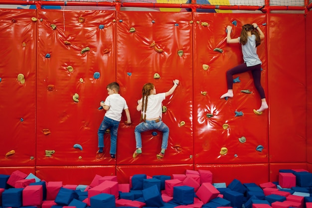 Crianças na parede de escalada no centro de entretenimento. Férias de meninos e meninas nos feriados, felicidade infantil, crianças felizes no parquinho