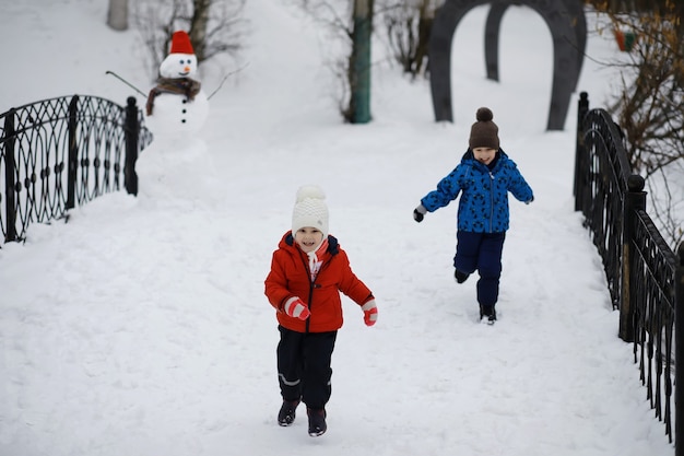 Crianças no parque no inverno. As crianças brincam com neve no parque infantil. Eles esculpem bonecos de neve e deslizam pelas colinas.