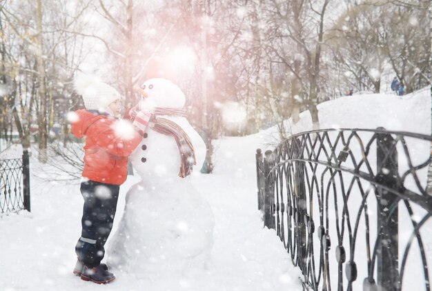Crianças no parque no inverno. As crianças brincam com neve no parque infantil. Eles esculpem bonecos de neve e deslizam pelas colinas.