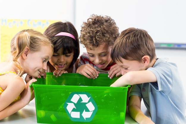 Crianças olhando garrafas de plástico em caixa de reciclagem