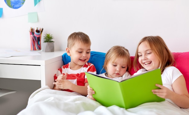 Foto crianças pequenas a ler um livro na cama em casa.