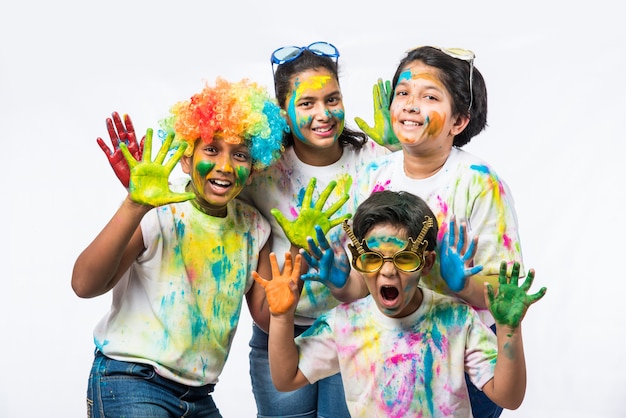 Crianças pequenas, amigos ou irmãos indianos celebrando o festival Holi com gulal ou cor de pó, doces, pichkari ou spray, isolado sobre fundo branco