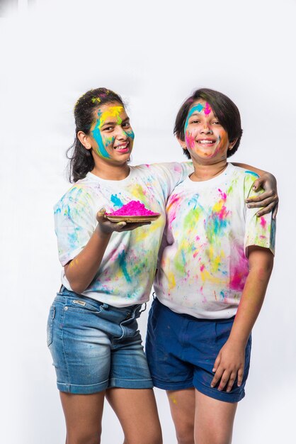 Crianças pequenas, amigos ou irmãos indianos celebrando o festival Holi com gulal ou cor de pó, doces, pichkari ou spray, isolado sobre fundo branco