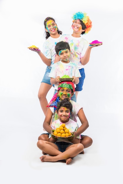 Crianças pequenas, amigos ou irmãos indianos celebrando o festival Holi com gulal ou cor de pó, doces, pichkari ou spray, isolado sobre fundo branco