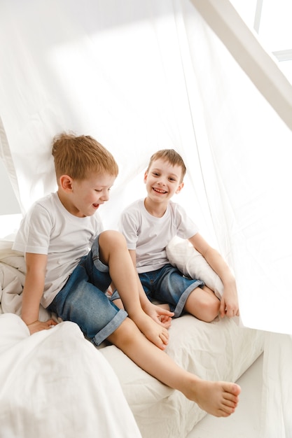 Crianças pequenas brincando na cama e se divertindo em uma cabana de lençol.