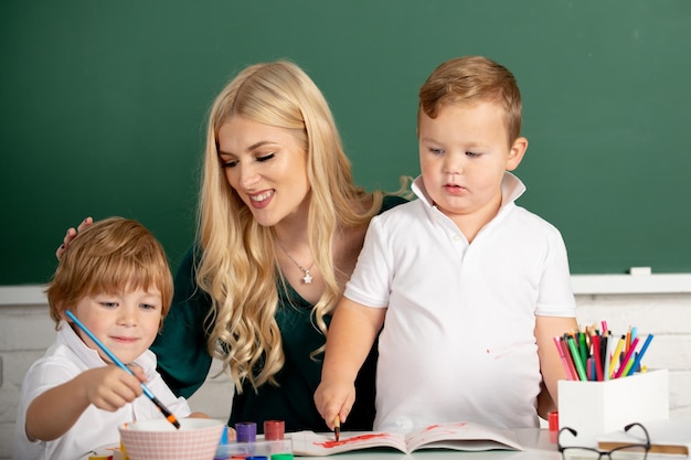 Crianças pequenas com professor de jardim de infância desenhando à mesa dentro de casa aprendendo e jogando ajuda de professor