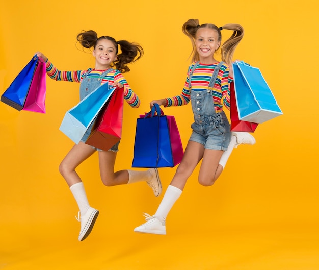 Crianças pequenas com sacolas de compras pesadas grande venda de presentes crianças viciadas em compras felizes meninas pacotes de cuidados salto livre Compras de verão Conceito de consumidor comprador Economia de compra de férias