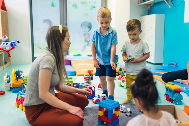 Crianças pequenas e sua professora de berçário brincando com blocos de construção de plástico e brinquedos de carros coloridos em um