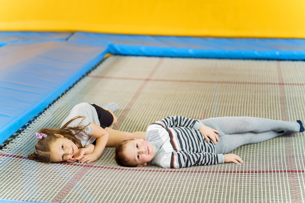 Crianças pequenas sorridentes felizes deitado no trampolim indoor no centro de entretenimento