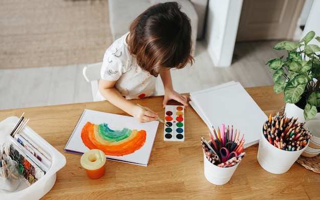 Crianças pintando arco-íris em aquarela à mesa em casa