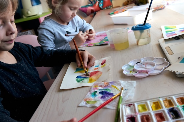 Crianças pintando quadros com aquarela durante a aula de arte. Os alunos estão se concentrando em desenhar com pincel. Paleta e roda de cores em aquarela. Aulas de hobby para iniciantes de teoria da cor.