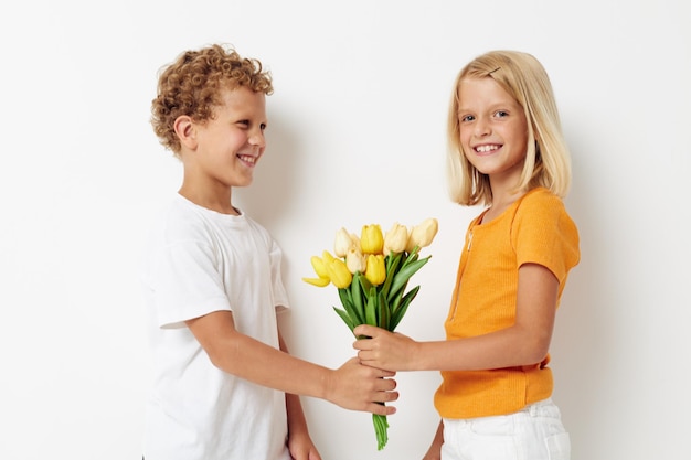 Crianças pré-escolares bonitas com um buquê de flores presente de aniversário férias fundo claro de infância