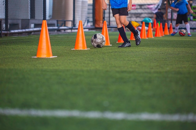 Foto crianças que jogam o cone de táticas de bola de futebol de controle no campo de grama com fundo de treinamento.