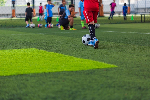 Crianças que jogam o cone de táticas de bola de futebol de controle no campo de grama com fundo de treinamento.