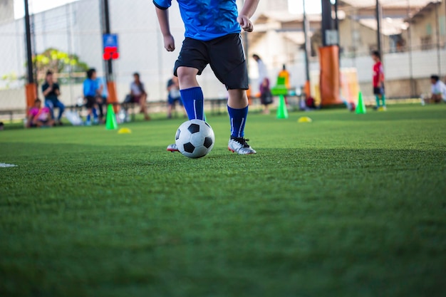 Crianças que jogam o cone de táticas de bola de futebol de controle no campo de grama com fundo de treinamento.