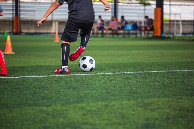 Crianças que jogam o cone de táticas de bola de futebol de controle no campo de grama com fundo de treinamento.