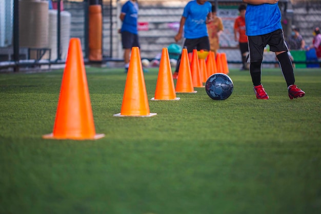 Foto crianças que jogam o cone de táticas de bola de futebol de controle no campo de grama com fundo de treinamento.