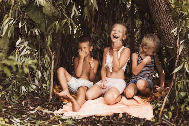 Crianças rindo brincam em uma cabana feita de galhos e folhas. Casa de madeira na aldeia