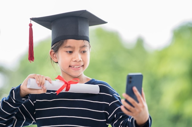 Crianças se formam com chapéu de formatura e certificado de graduação enrolado segurando um smartphone para ligar