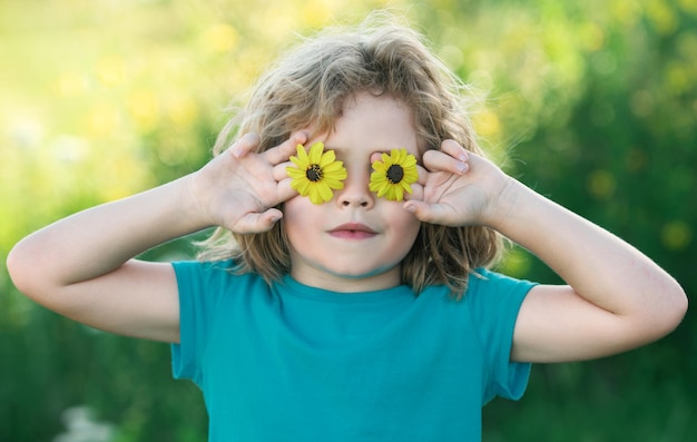 Crianças segurando flores na frente dos olhos aproveitando o verão Crianças encaram retrato de menino Humor de verão