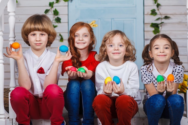 Foto crianças segurando ovos de páscoa. lindas crianças sentam-se perto da cesta com tulipas e seguram ovos de páscoa nas mãos. momentos engraçados