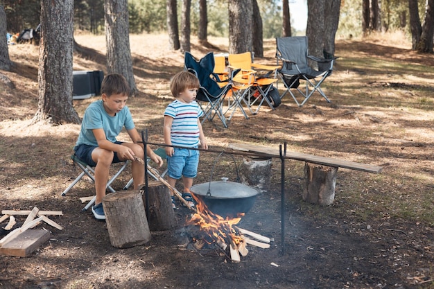 Crianças sentadas ao redor de uma fogueira na floresta no verão Piquenique em família ao ar livre Vida de acampamento Cozinhando no caldeirão em chamas na natureza