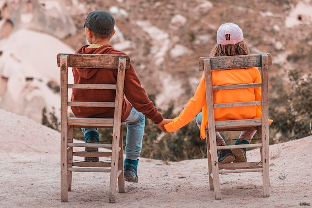 Crianças sentadas em cadeiras de madeira de mãos dadas