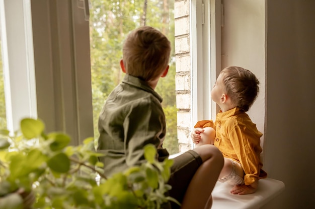 Crianças sentadas no parapeito da janela e esperando alguém chegando Dois irmãos amigos Crianças pré-escolares fofas sozinhas em casa Meninos estão esperando por sua mãe ou pai Solidão Pais ocupados