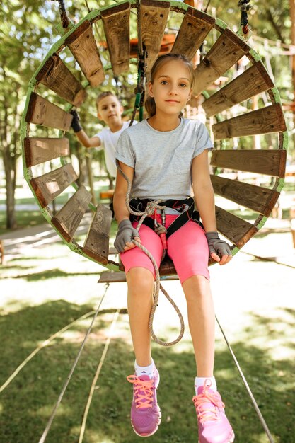 Crianças sorridentes em equipamentos sobem no parque de corda, playground. crianças subindo em ponte suspensa