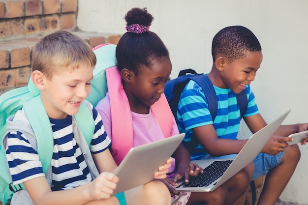 Crianças sorridentes usando um laptop e tablet digital nas escadas