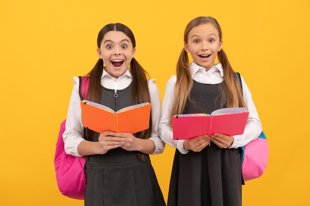 Crianças surpresas em uniformes formais leem livros escolares fundo amarelo, biblioteca.