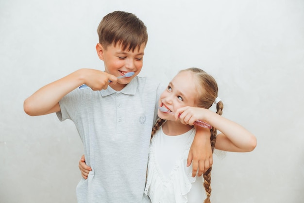 Crianças, um menino e uma menina, escovam os dentes e riem isolados em um fundo branco, higiene odontológica pediátrica e limpeza dos dentes