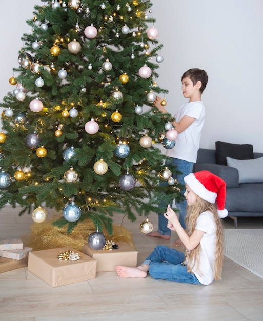 Crianças - um menino e uma menina estão brincando perto da árvore de Natal. Interior da sala de estar com árvore e decorações de Natal. Ano Novo. Doação de presente.