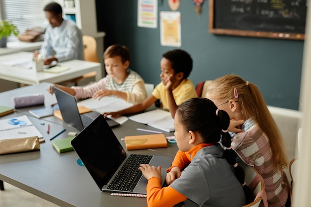 Crianças usando laptops em pares sentadas na mesa na sala de aula na escola
