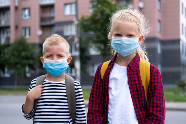 Crianças usando máscara e mochilas protegem e protegem contra o coronavírus na volta às aulas. irmão e irmã indo para a escola após o fim da pandemia.