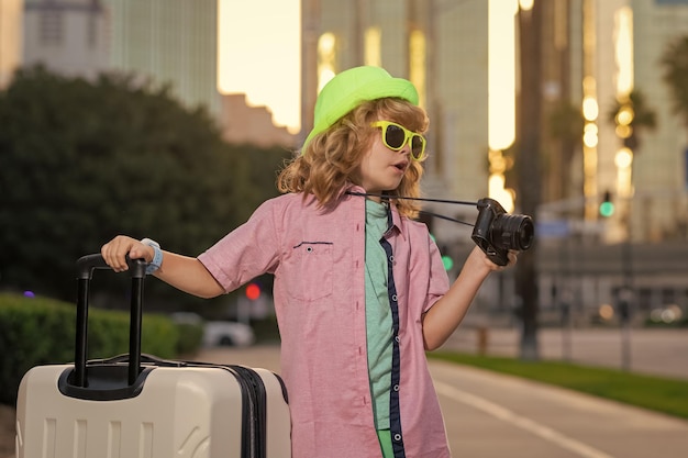 Crianças viajam criança feliz menino carregando malas de viagem ao ar livre na rua da cidade estilo de vida de viagem e