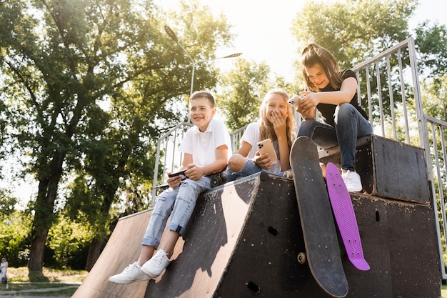 Crianças viciadas em telefone com pranchas de skate e penny sorrindo e olhando para smartphones na rampa de esportes no playground vício de crianças em telefones