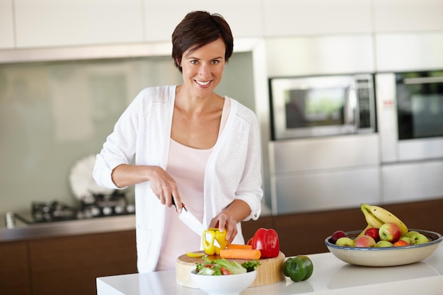 Criando um prato delicioso do zero retrato de uma mulher atraente cortando legumes no balcão da cozinha