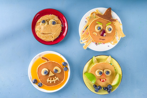 Foto criativas panquecas caseiras de halloween no café da manhã, em forma de monstros engraçados, fantasma, morcego, bruxa. com doces ou travessuras tradicionais, doces e decorações, vista de cima sobre fundo azul colorido