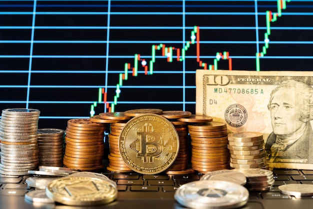 Criptomonedas Bitcoin, ethereum y cardano y varias monedas y un billete de dólar delante del gráfico del mercado de valores en un teclado