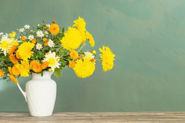 Crisântemo amarelo e branco em jarro branco na mesa de madeira