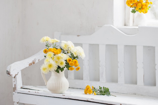 Crisantemos amarillos en jarra en el viejo banco de madera blanca