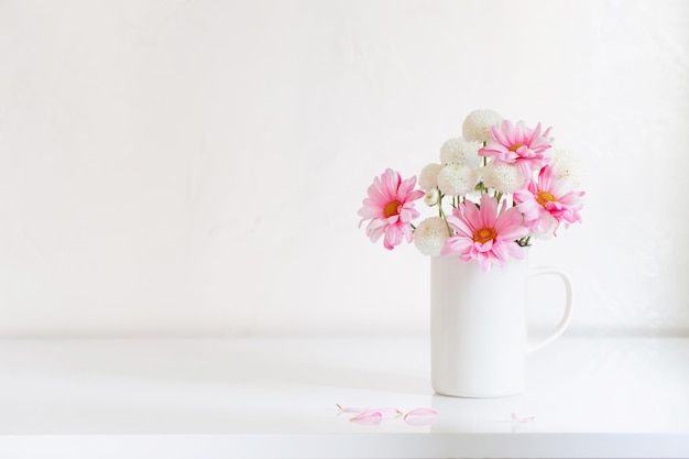 Crisântemos brancos e rosa em copo vintage em fundo branco