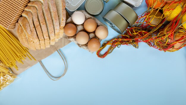 Crise de abastecimento de alimentos estoque de alimentos para o período de isolamento de quarentena. Alimentos enlatados, trigo sarraceno, massas, ovos, frutas sobre um fundo azul. Copie o espaço para o texto.