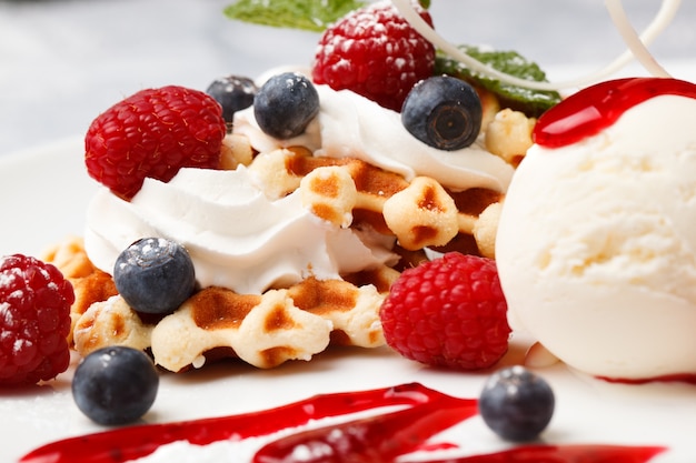 Crispy Golden Waffeln werden mit Sahne, Vanilleeis und frischen Blaubeeren serviert