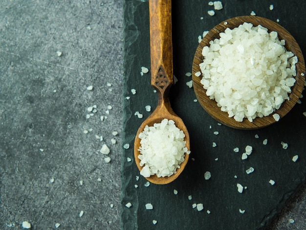 Cristais de sal marinho em uma colher de pau e tigela sobre uma mesa escura