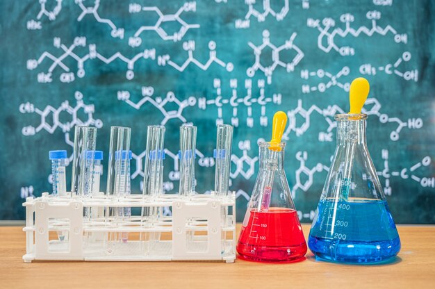 Cristalería de laboratorio con fondo de pizarra con diversas fórmulas químicas