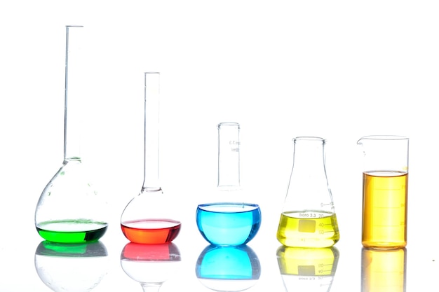 Cristalería de laboratorio con líquidos coloreados sobre mesa reflectante sobre blanco