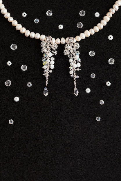 Cristales de aretes de bisutería de boda hechos a mano, collar de perlas blancas, fondo negro de vista plana superior